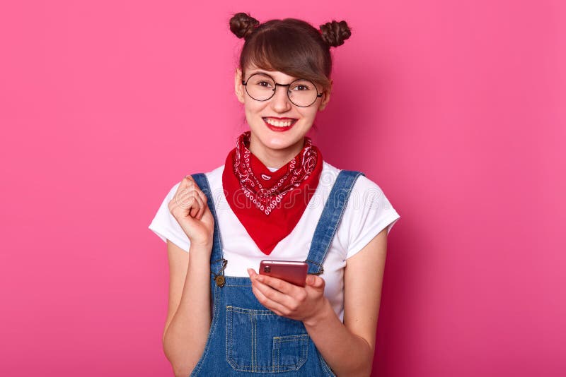 Photo of happy young teenager female with bunches, glasses, bandana on nack, dressed denim overalls and white t shirt, looks royalty free stock image Photo of happy young teenager female with bunches, glasses, bandana on nack, dressed denim overalls and white t shirt, looks royalty free stock image