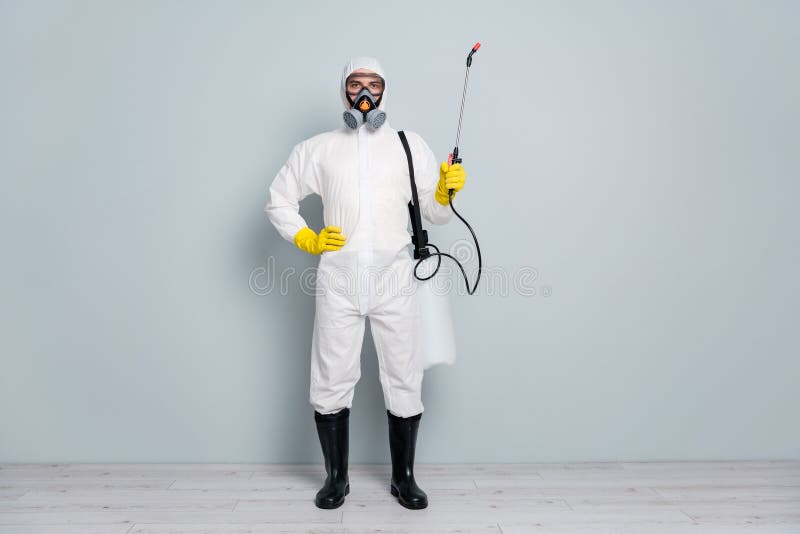 Full length photo of epidemic professional guy disinfectant start cleaning, surface public places during pandemic hold sprayer wear white hazmat protective suit isolated grey color background. Full length photo of epidemic professional guy disinfectant start cleaning, surface public places during pandemic hold sprayer wear white hazmat protective suit isolated grey color background