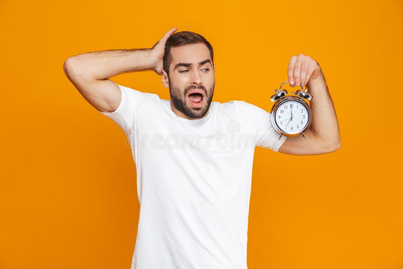 Photo of irritated man 30s in casual wear holding alarm clock, isolated over yellow background royalty free stock images Photo of irritated man 30s in casual wear holding alarm clock, isolated over yellow background royalty free stock images