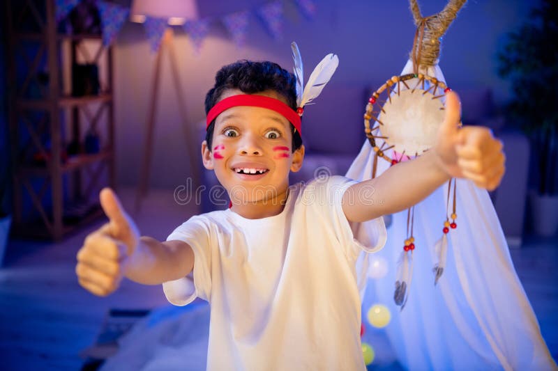 Photo of joyful surprised boy in native american costume have theme party birthday thumb up symbol in evening playroom stock images