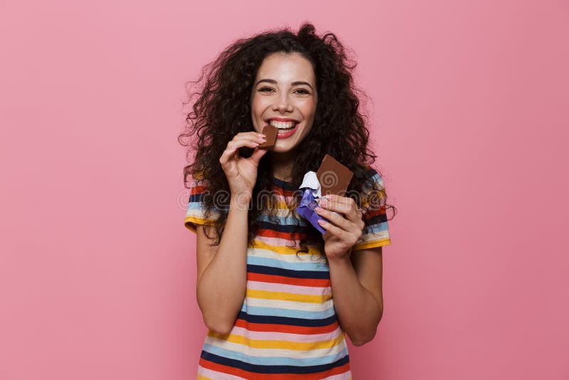 Photo of lovely woman 20s with curly hair eating chocolate bar