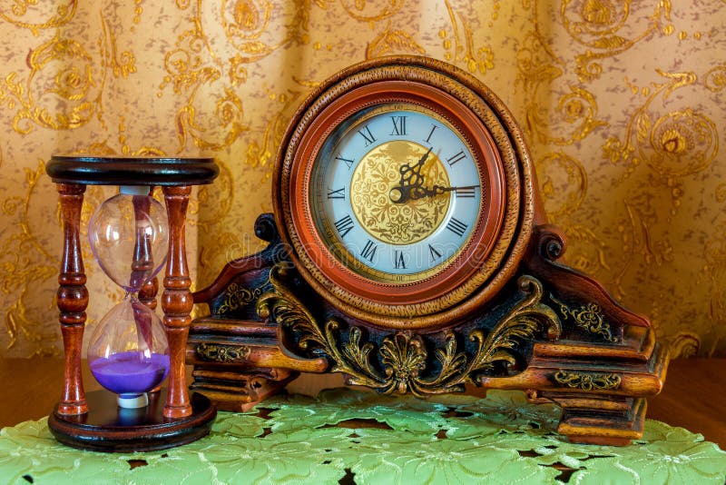 Photo of an old clock and sandglass on brown background