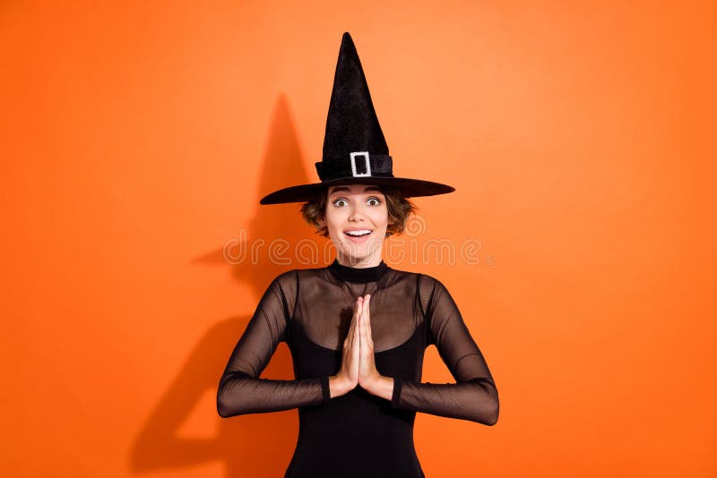 Photo portrait of nice young girl hold palms together excited ask wear stylish black halloween witch clothes isolated on orange background. Photo portrait of nice young girl hold palms together excited ask wear stylish black halloween witch clothes isolated on orange background.