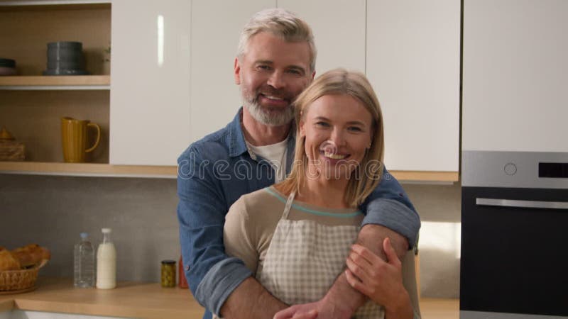 Photo prise adulte famille caucasienne couple à la maison cuisine câlin câliner sourire à la caméra. portrait moyen banque de vidéos