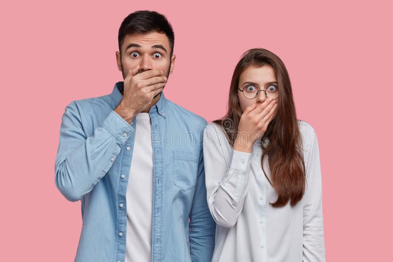 Photo of scared speechless lady and man cover mouthes with palms, have stupefied expressions, dressed in elegant shirt