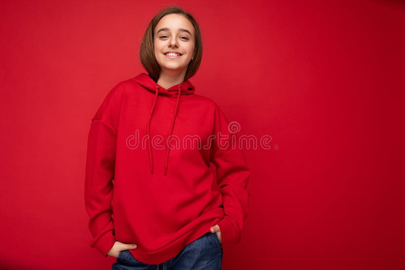 Photo shot of beautiful positive smiling brunette little girl wearing stylish red hoodie standing isolated over red