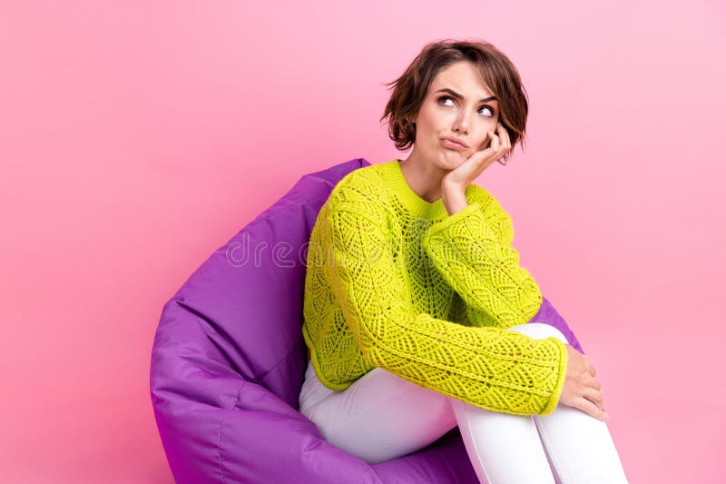 Photo of suspicious unsure girl dressed neon sweater sitting bean bag arm cheek looking empty space isolated pink color