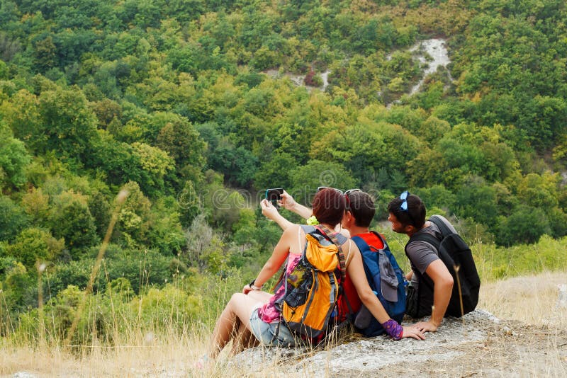 Photo of two men and woman taking selfie while sitting on hillside with vegetation royalty free stock photography Photo of two men and woman taking selfie while sitting on hillside with vegetation royalty free stock photography