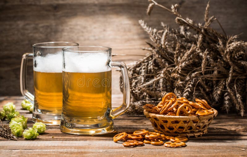 Photo of two mugs, beer with pretzels, wheat spikes, hops
