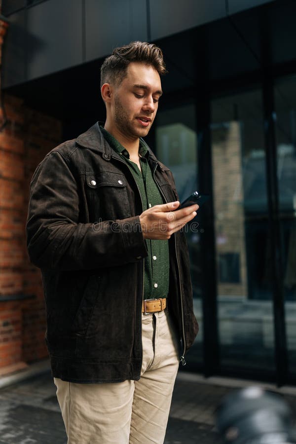 Photo verticale d'un homme costumé debout dans la rue de la ville à l'aide d'un smartphone pour vérifier les messages naviguer sur photographie stock libre de droits