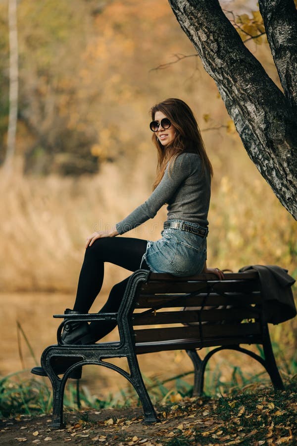 Photo of woman in sunglasses sitting on bench in autumn park