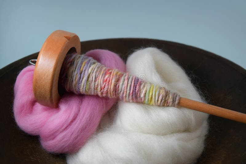 This is a photo of a wooden spindle with colorful hand spun yarn in a wooden bowl full of wool roving bundles. This is a photo of a wooden spindle with colorful hand spun yarn in a wooden bowl full of wool roving bundles