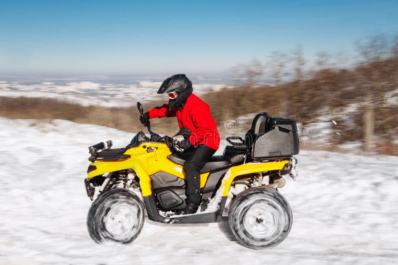 Photo of young extremal driver in red warm winter clothes and black helmet drive his ATV 4wd quad bike stand in heavy