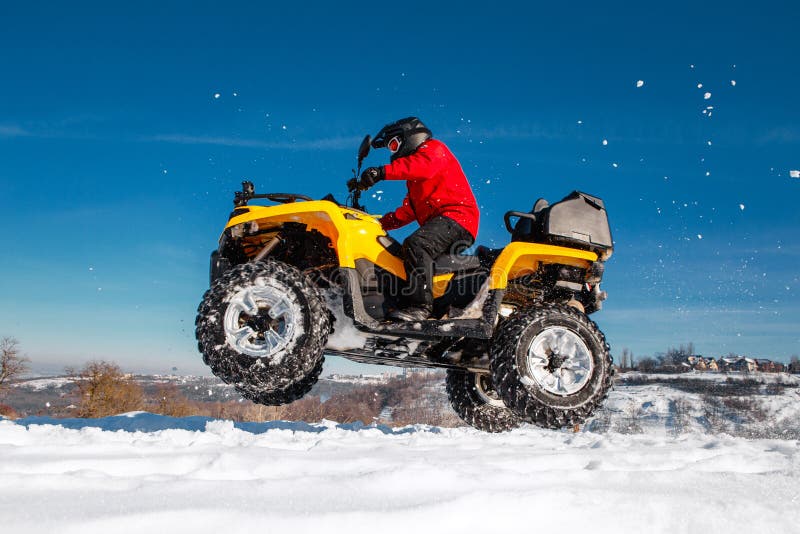 Photo of young extremal driver in red warm winter clothes and black helmet jump in the air with the ATV 4wd quad bike