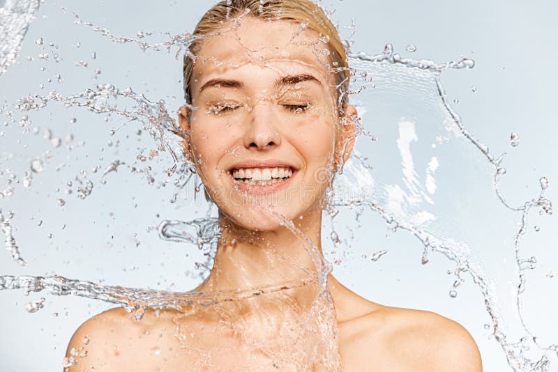 Photo of  young  woman with clean skin and splash of water. Portrait of smiling woman with drops of water around her face. Spa