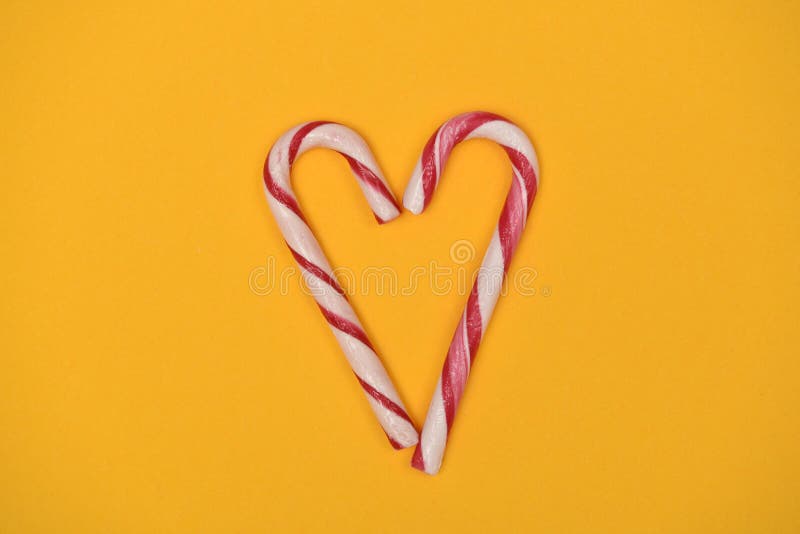 Photograph of 2 peppermint candy canes put together to form a heart on a yellow background. Photograph of 2 peppermint candy canes put together to form a heart on a yellow background