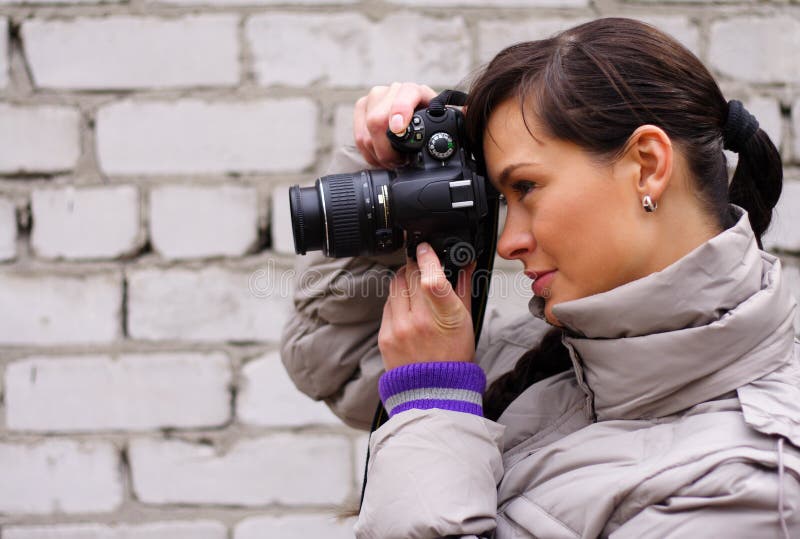 Žena fotograf na pozadí cihlové zdi.