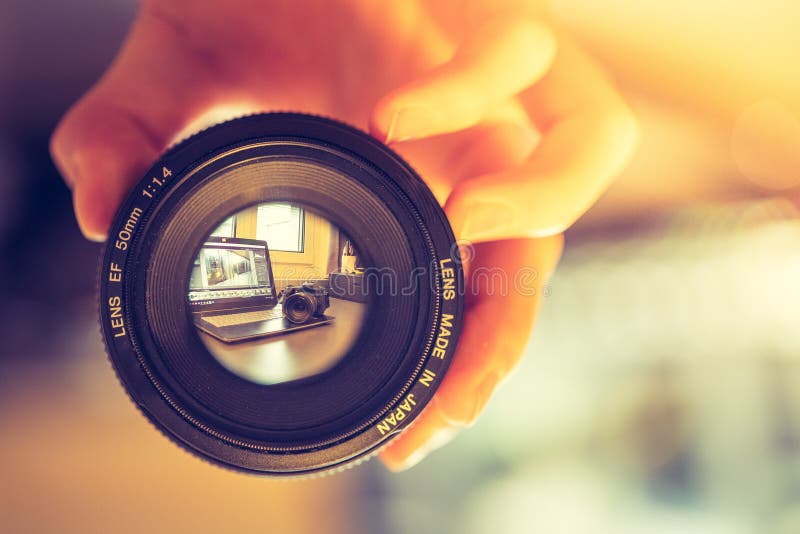 Photographer is holding a photography lens in his hand, laptop in the blurry background