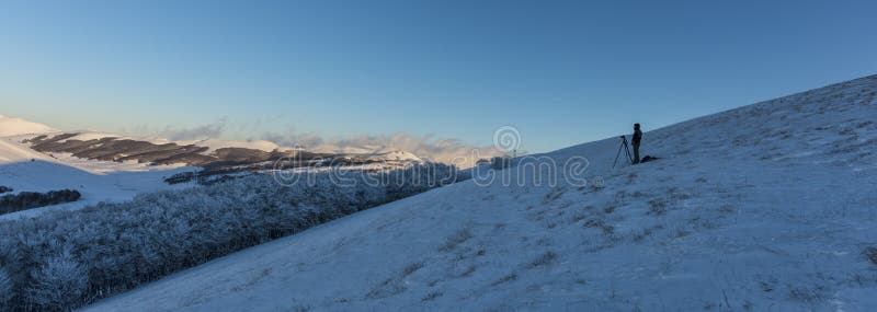 Photographer standing alone on a hill with snow at sunset, Sibillini mountains, Umbria, Italy