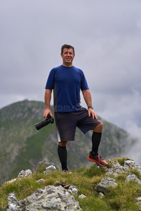 Photographer standing on mountain summit man holding camera grassy under cloudy sky fotografia de stock royalty free