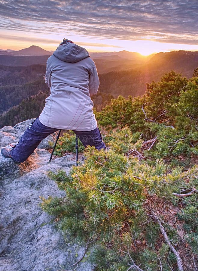 Photographer is taking pictures with camera in morning hills. Nature landscape photographer with photo equipment on rock. Silhouette of hiker woman