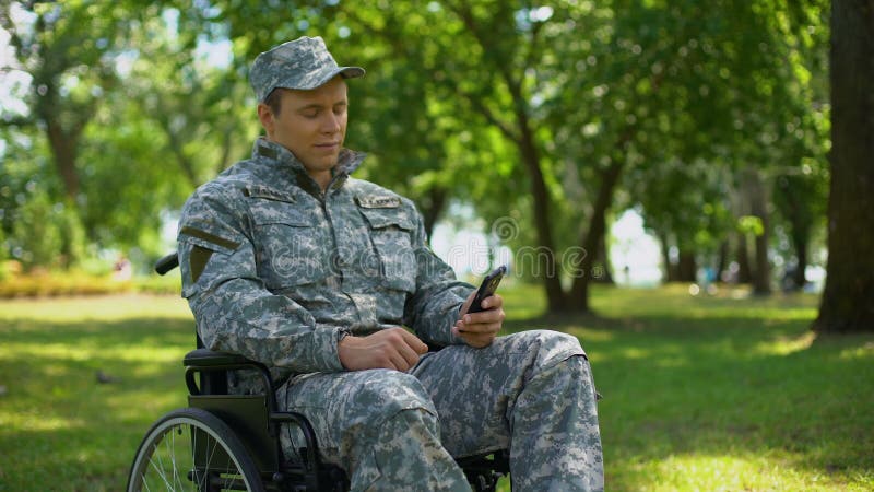 Photos handicapées de smartphone de défilement de militaire, repos en parc de ville, nostalgie