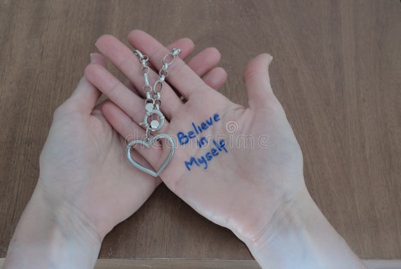 Phrase BELIEVE IN MYSELF written on the palm of a woman`s hand holding a silver bracelet with a heart royalty free stock images