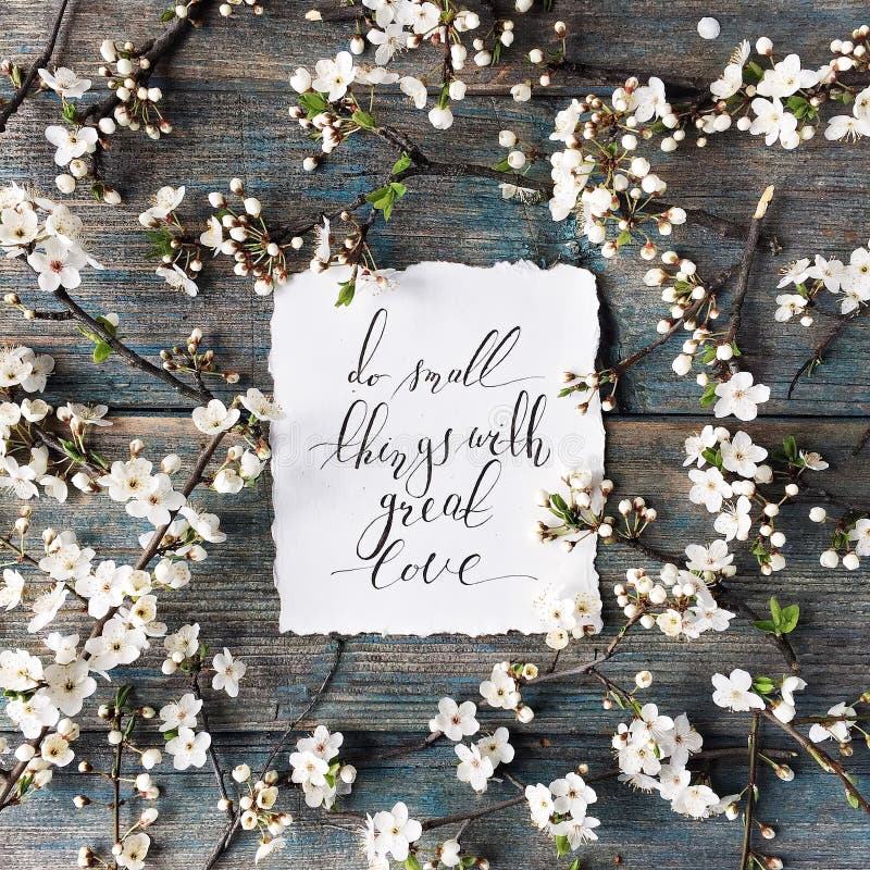 Phrase `Do small things with great love` written in calligraphy style on paper with wreath frame. With white flowers and branches isolated on old retro wooden royalty free stock photography