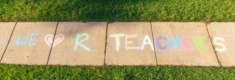 The phrase `We Love Our Teachers` written with sidewalk chalk, on gray concrete pavement background