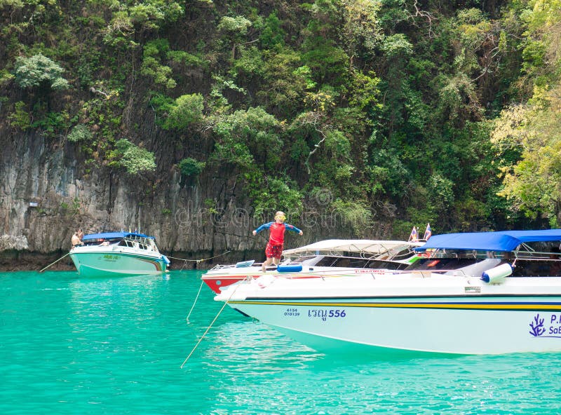 Phuket, Tailândia - 27 de março de 2019: Um rapaz pequeno em um maiô e em uns saltos nadadores dos óculos de proteção de um barco imagem de stock royalty free Phuket, Tailândia - 27 de março de 2019: Um rapaz pequeno em um maiô e em uns saltos nadadores dos óculos de proteção de um barco imagem de stock royalty free