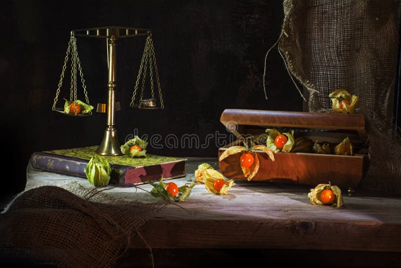 Physalis fruits escape from a jewelery box to a brass scale, still life metaphor on a rustic wooden table in front of a dark