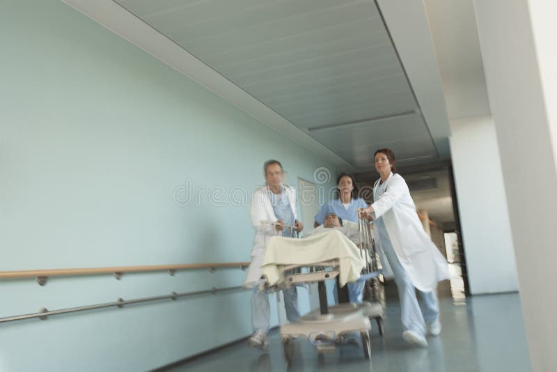 Physicians Rushing Patient On Gurney Down Hospital Corridor Stock Image