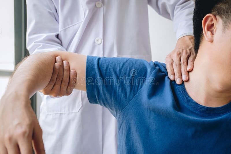 Physioth?rapeute de docteur aidant un patient masculin tout en donnant exer?ant le traitement massant l'?paule du patient dans un photos libres de droits Physioth?rapeute de docteur aidant un patient masculin tout en donnant exer?ant le traitement massant l'?paule du patient dans un photos libres de droits