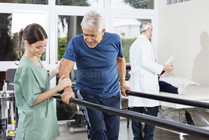 Physiotherapeut Standing By Patient, das zwischen parallele Stange geht stockfoto Physiotherapeut Standing By Patient, das zwischen parallele Stange geht stockfoto