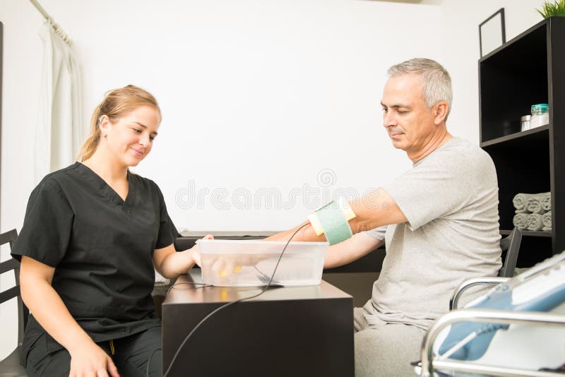 Young physiotherapist giving electrotherapy to mature patient at table in hospital. Young physiotherapist giving electrotherapy to mature patient at table in hospital