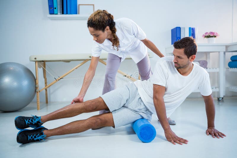 Physiotherapist Doing Leg Therapy To a Man Using Foam Roll Stock Photo