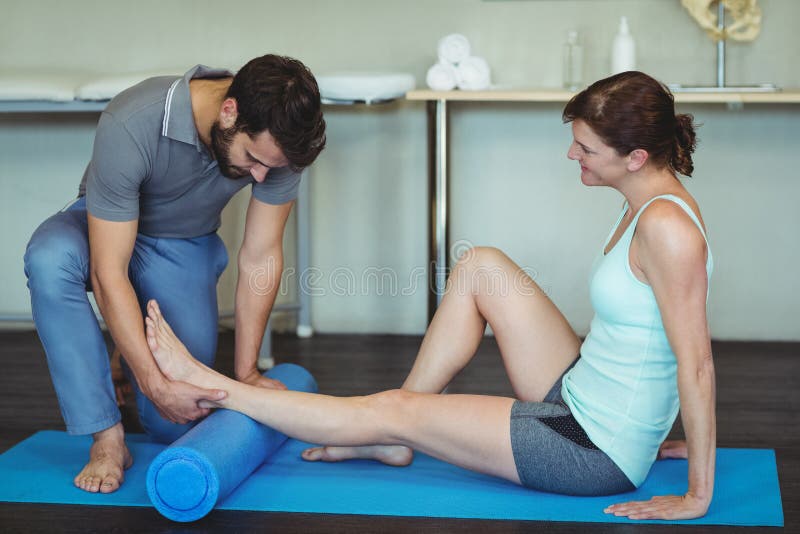 Physiotherapist giving leg massage to a woman on exercise mat
