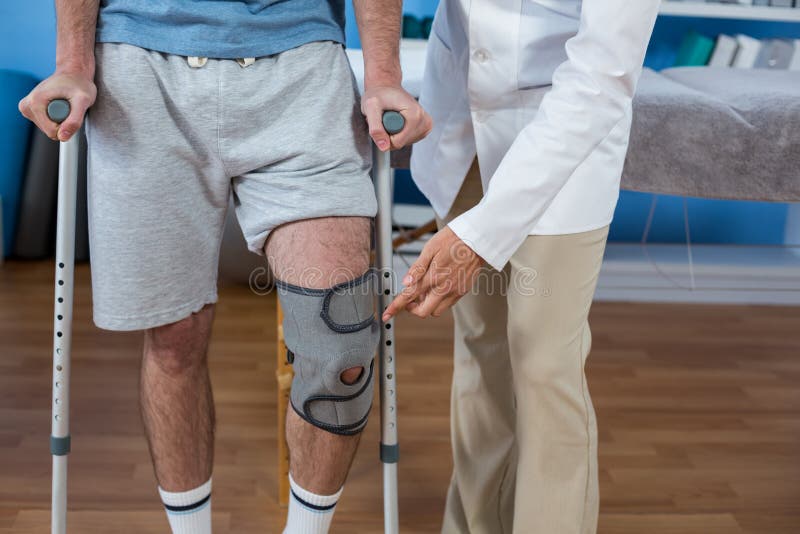 Physiotherapist Helping Patient To Walk with Crutches Stock Photo