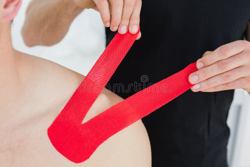 Physiotherapist putting on red kinesio tape on patients shoulder royalty free stock image