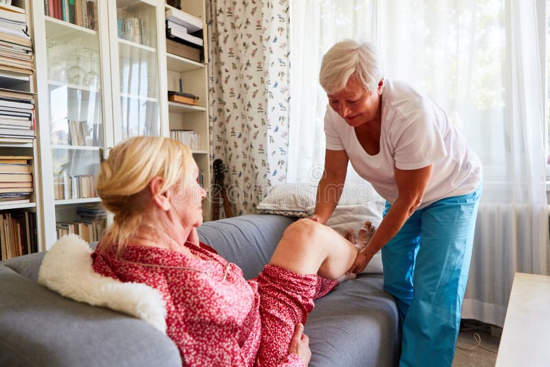 Physiotherapist treating a senior citizen`s knee on the sofa in home care. Physiotherapist treating a senior citizen`s knee on the sofa in home care