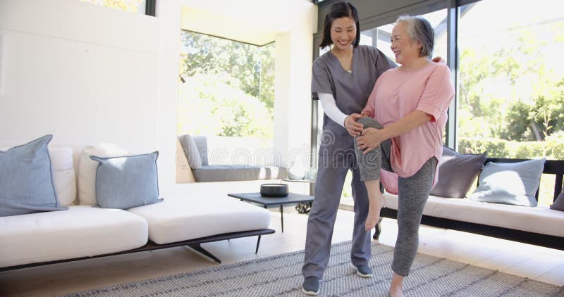 Physiothérapeute aidant la femme asiatique âgée à faire un exercice de jambe dans le salon clips vidéos