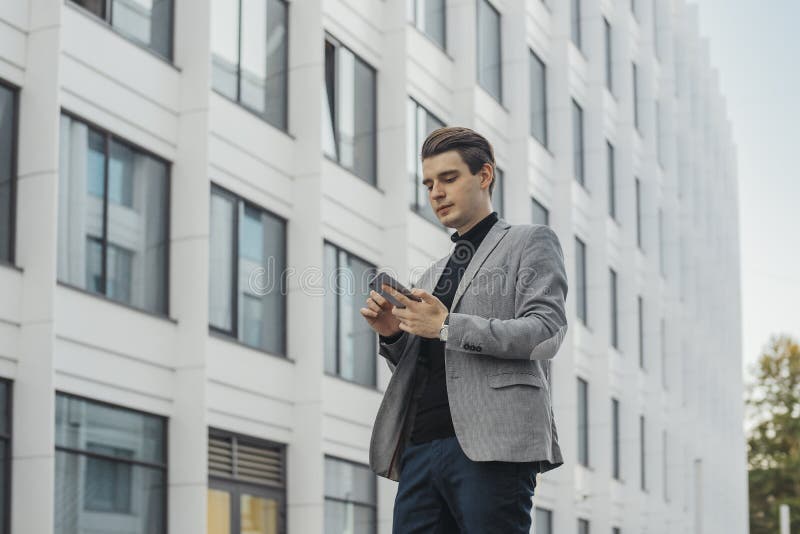 Piano distante di giovane uomo d'affari che parla dal telefono cellulare accanto al grattacielo fotografie stock Piano distante di giovane uomo d'affari che parla dal telefono cellulare accanto al grattacielo fotografie stock