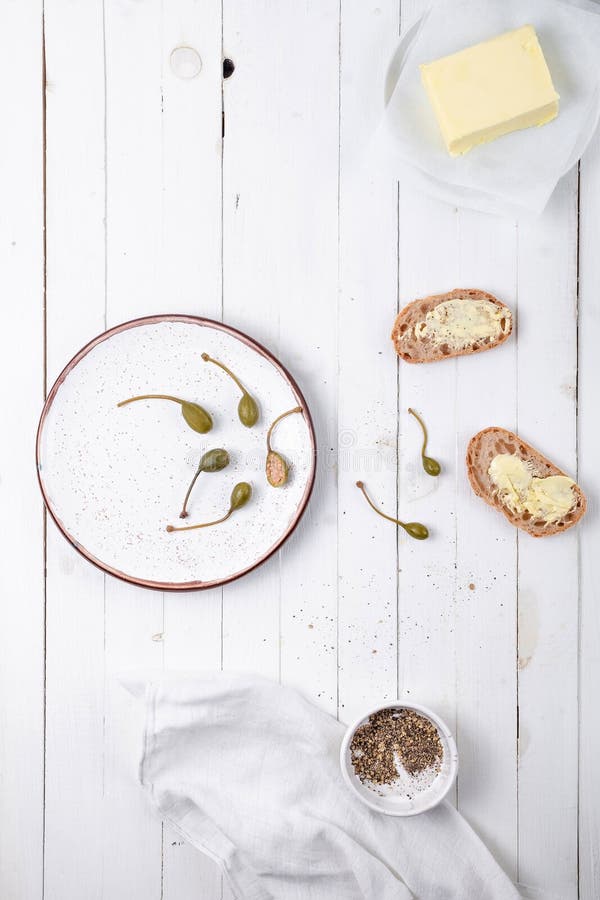 Piatto bianco con i capperi, il pane con burro e le spezie su un fondo di legno bianco, vista superiore fotografia stock Piatto bianco con i capperi, il pane con burro e le spezie su un fondo di legno bianco, vista superiore fotografia stock