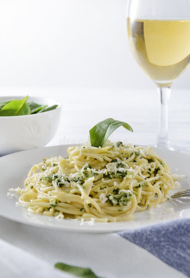 1 plate of pasta, spaghetti with spinach and cheese, a glass of wine on a white wooden background close up. 1 plate of pasta, spaghetti with spinach and cheese, a glass of wine on a white wooden background close up