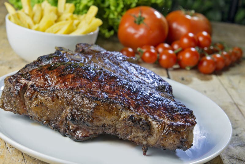 Piatto rotondo con la bistecca di manzo arrostita della lombata sulla tavola di legno fotografia stock Piatto rotondo con la bistecca di manzo arrostita della lombata sulla tavola di legno fotografia stock
