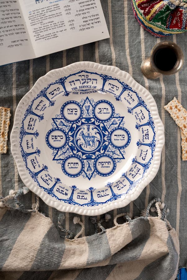 Vintage traditional passover plate, used during the Jewish holiday is show with the habbadah, kiddush cup and colourful yarmulke or kippa in background. The hebrew writing on the plate mirrors the English words i.e. bitter herb. Vintage traditional passover plate, used during the Jewish holiday is show with the habbadah, kiddush cup and colourful yarmulke or kippa in background. The hebrew writing on the plate mirrors the English words i.e. bitter herb.