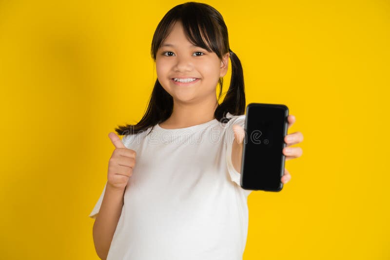 Piccola asiatica mostra una schermata vuota del telefono cellulare e si arrampica sulla parete gialla dello studio fotografie stock libere da diritti