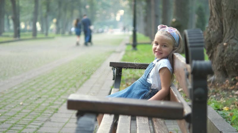 Piccola bambina felice seduta su una panchina al parco estivo archivi video