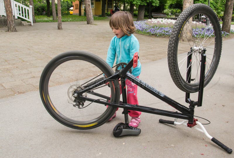 Piccola bella ragazza che ripara bici in parco fotografia stock