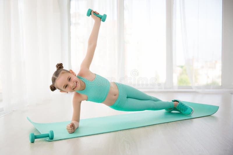 Piccola ginnasta sportiva della ragazza in abiti sportivi che fanno gli esercizi su una stuoia dell'interno fotografie stock Piccola ginnasta sportiva della ragazza in abiti sportivi che fanno gli esercizi su una stuoia dell'interno fotografie stock
